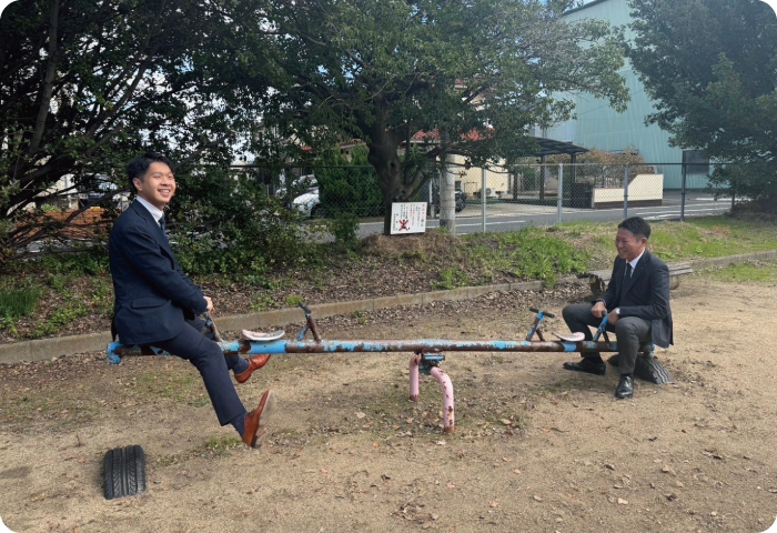 公園のシーソーにスーツの二人が遊んでいる写真